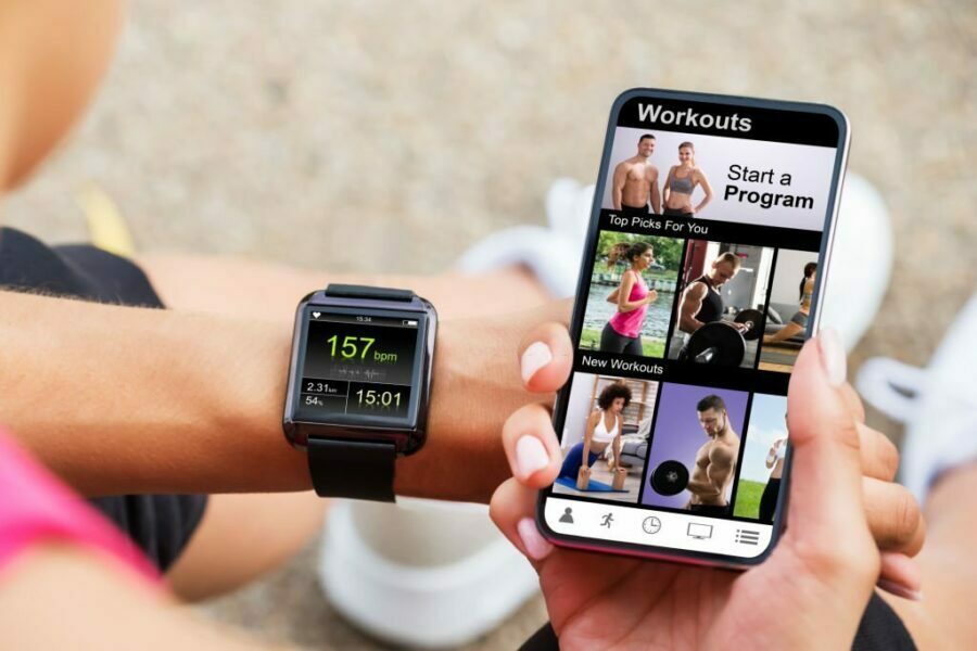 Femeie alergând și privind la ceasul inteligent și la telefonul ei pentru monitorizarea antrenamentului