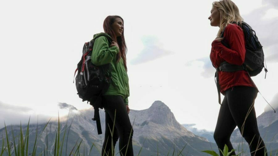 Două femei poartă jachete softshell dama și admiră lanțurile muntoase din depărtare.