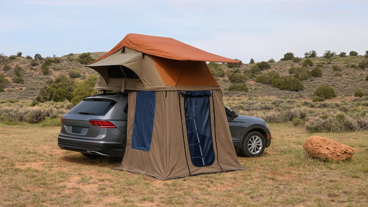 Cort de plafon auto cu anexă montat pe un SUV gri, într-un peisaj arid cu dealuri și vegetație joasă.