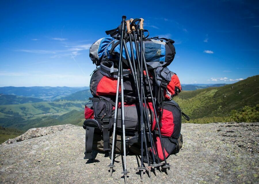 Rucsac roșu plasat pe vârful unui munte, cu peisaj montan în fundal.