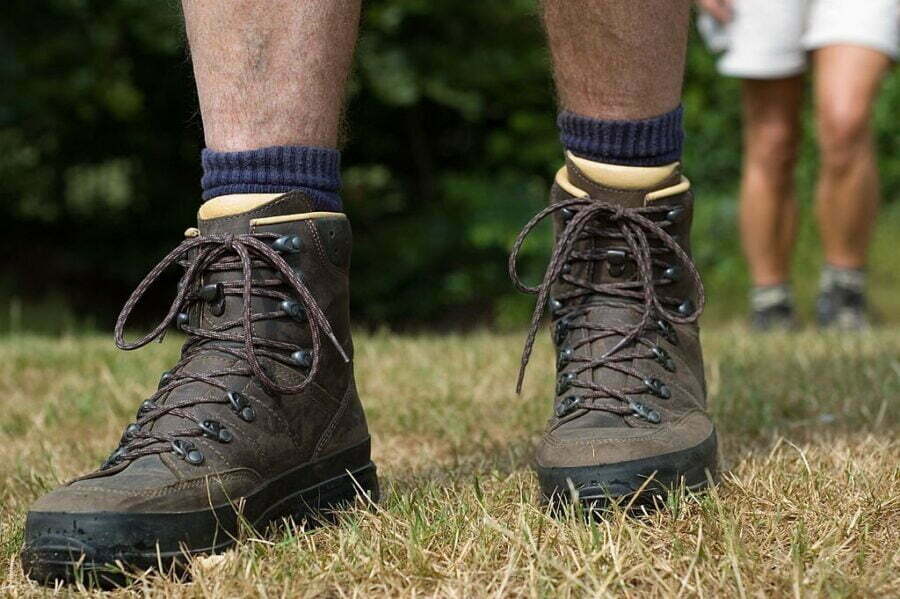 Bocanci de drumeție strânși pe un teren cu iarbă, cu șosete de drumeție de culoare închisă vizibile deasupra gleznelor.