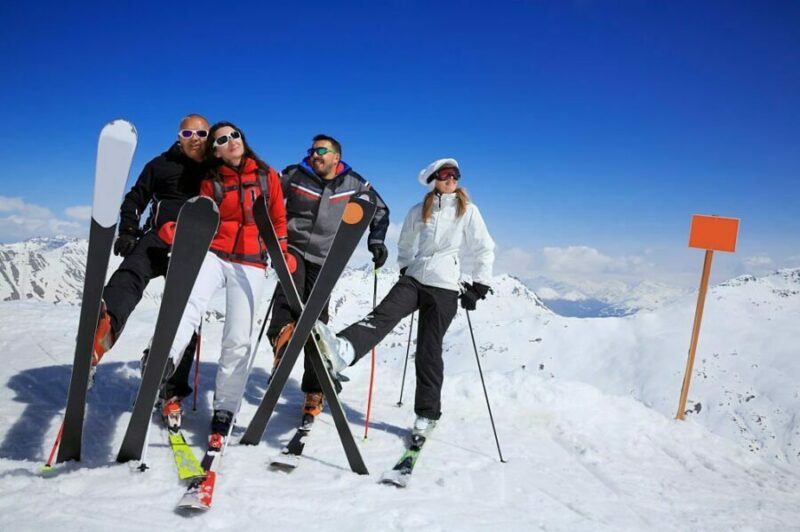 Grup de schiori cu schiuri de tură pregătiți pentru aventură pe un vârf de munte însorit.