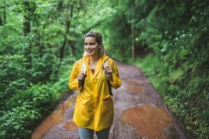 Tânără zâmbitoare care poartă o jachetă de ploaie pentru dame în timp ce merge prin pădurea udă după ploaie.