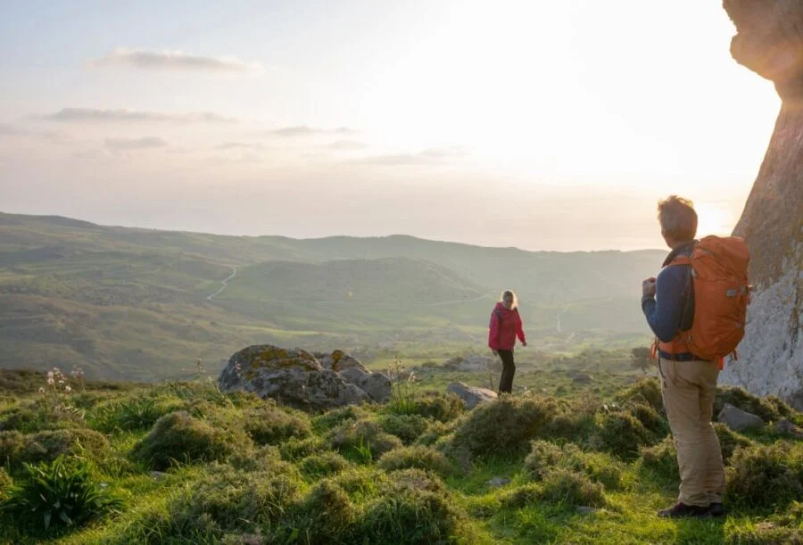 Doi drumeți care privesc spre un peisaj îndepărtat, purtând pantaloni convertibili și cu role-up pentru adaptabilitate la diverse condiții meteorologice și de teren