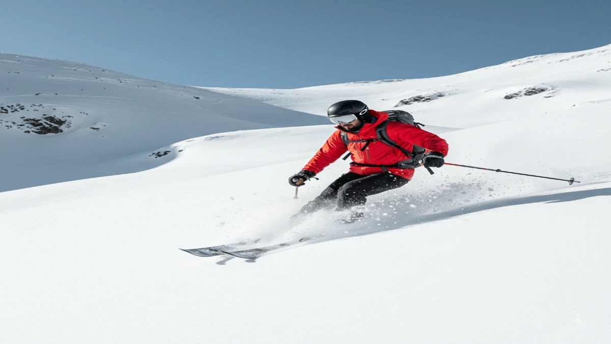Schior de ski touring coborând prin zăpadă powder pe o pantă montană deschisă