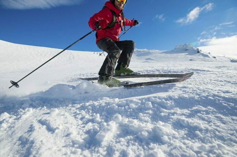 Schior în echipament roșu pe schiuri de tură traversând o zonă cu zăpadă proaspătă.