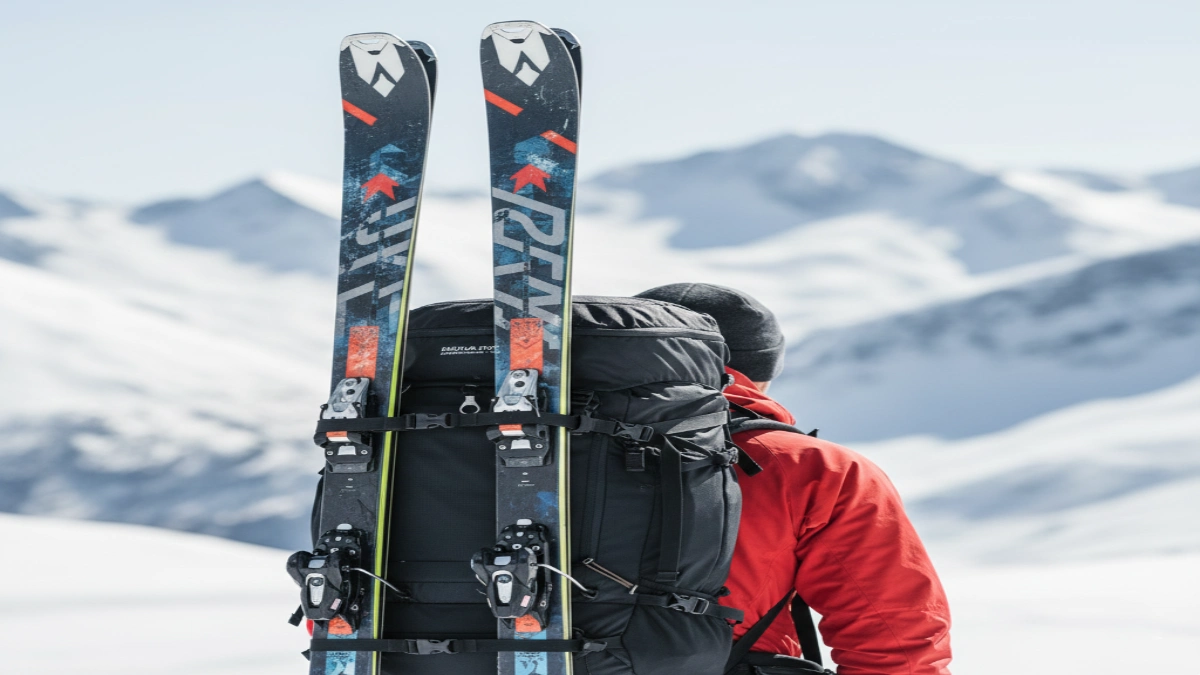 Schiuri de tură prinse pe rucsacul unui schior în peisaj montan de iarnă