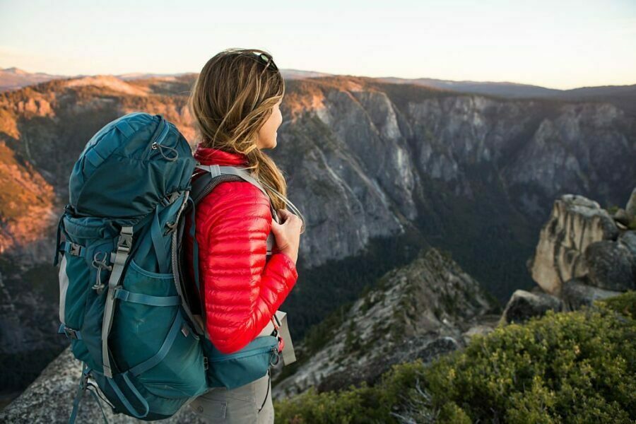 Femeie cu geacă de puf roșie privind peisajul muntos în timpul unei drumeții