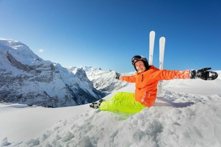 Schioare fericită în geacă de schi portocalie se relaxează pe zăpadă.