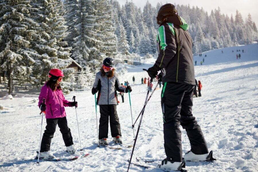 Instructor de schi și copii învățând să schieze folosind bețe de schi pe pârtie.