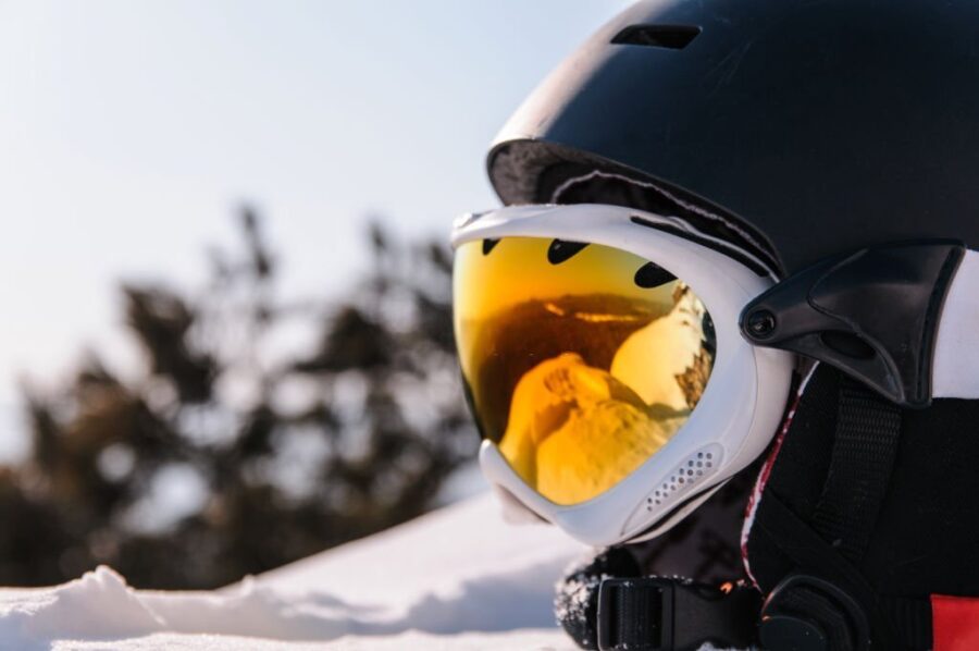 Casca de ski negră cu ochelari de protecție cu lentile galbene în lumina soarelui pe zăpadă