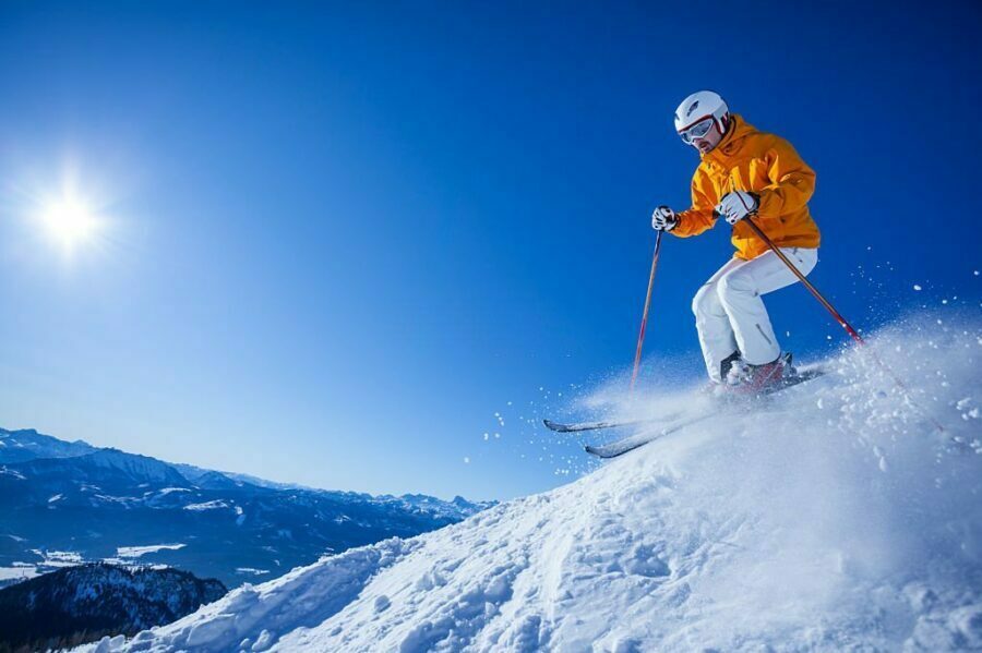 Schior bărbat cu pantaloni de ski galbeni în acțiune pe pârtie însorită