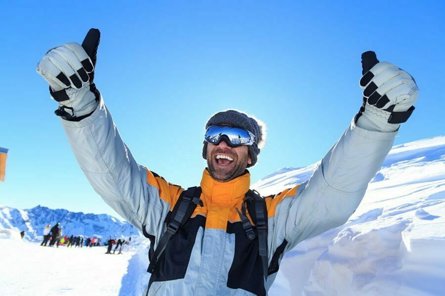 Schior entuziasmat cu brațele ridicate și geacă de ski galben cu gri