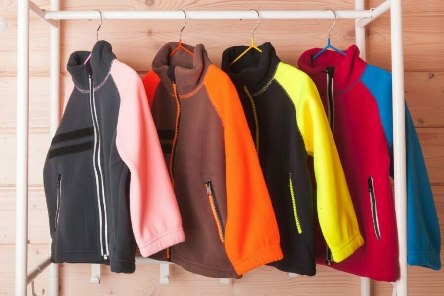 Colecție colorată de jachete fleece de damă atârnate pe umerașe.