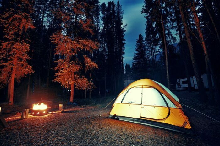 Imagine cu o tabără în pădure, unde se poate vedea un cort și un foc de tabără, în Parcul Național Banff.