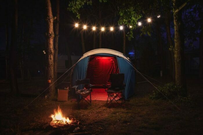 Imagine cu un cort în mijlocul pădurii, cu un foc aprins în apropiere, la miezul nopții.