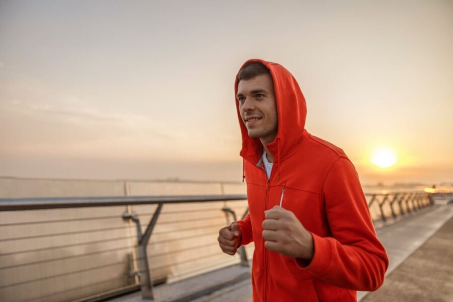 Tânăr sportiv zâmbitor purtând hanorac în timp ce aleargă pe pod