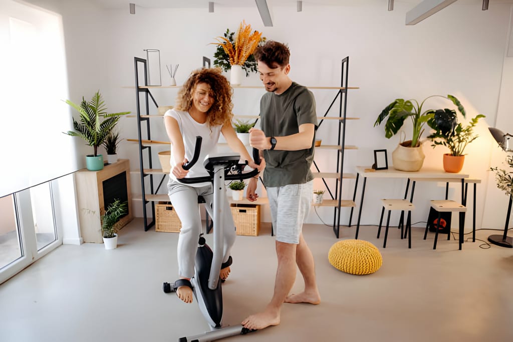 Cuplu vesel folosind bicicleta fitness într-un spațiu de locuit modern și luminos