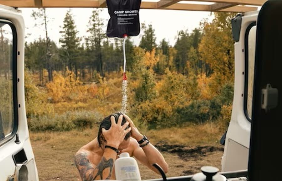Bărbat făcând duș în natură cu un duș portabil camping