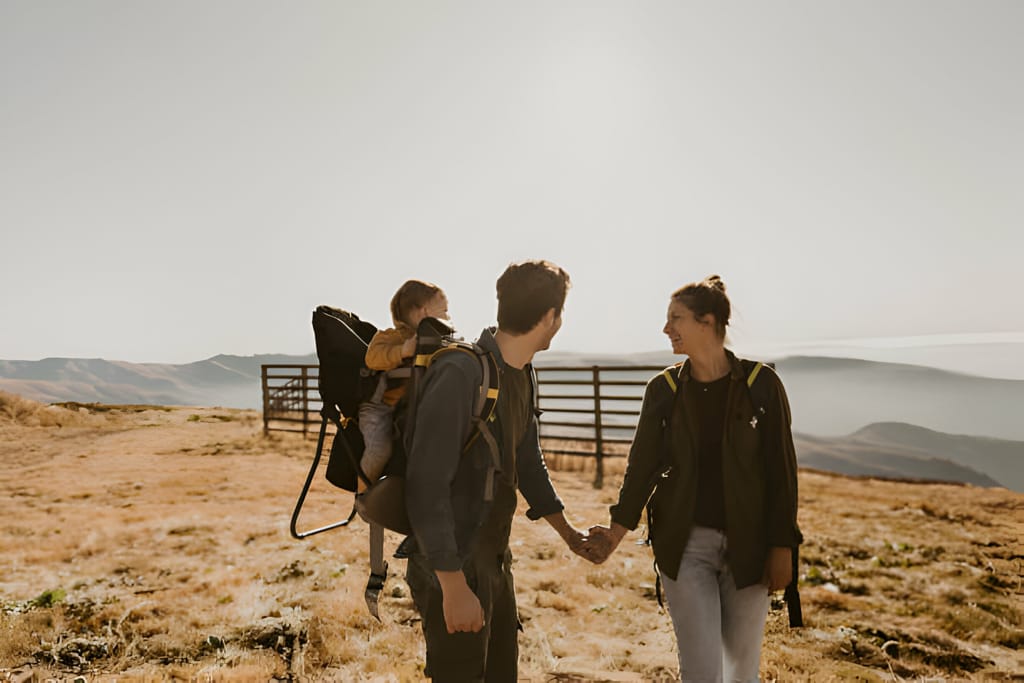 Familie pe un traseu montan cu tatăl purtând un rucsac de transport pentru copii.