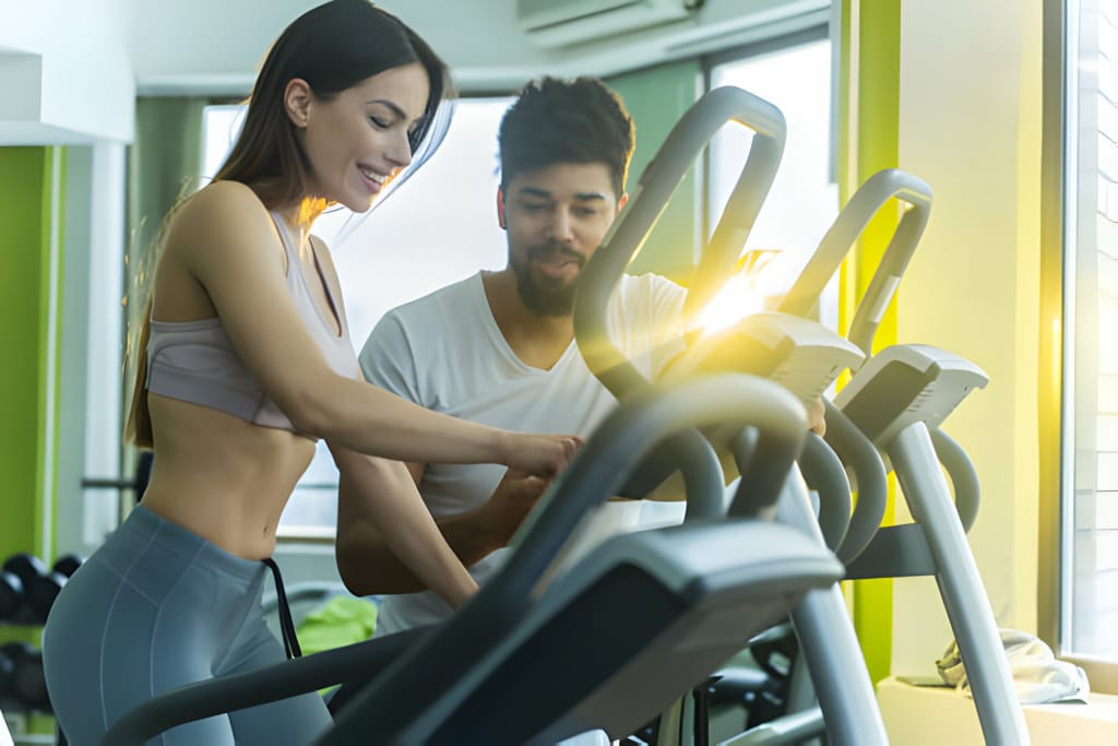 Un instructor ajută o clientă să folosească o bandă de alergat într-o sală de fitness luminoasă