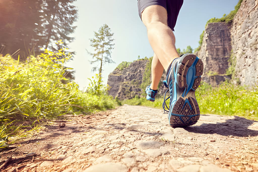 Pantofi de alergare pe trail în acțiune, pe un drum pietros cu vegetație și stânci în fundal