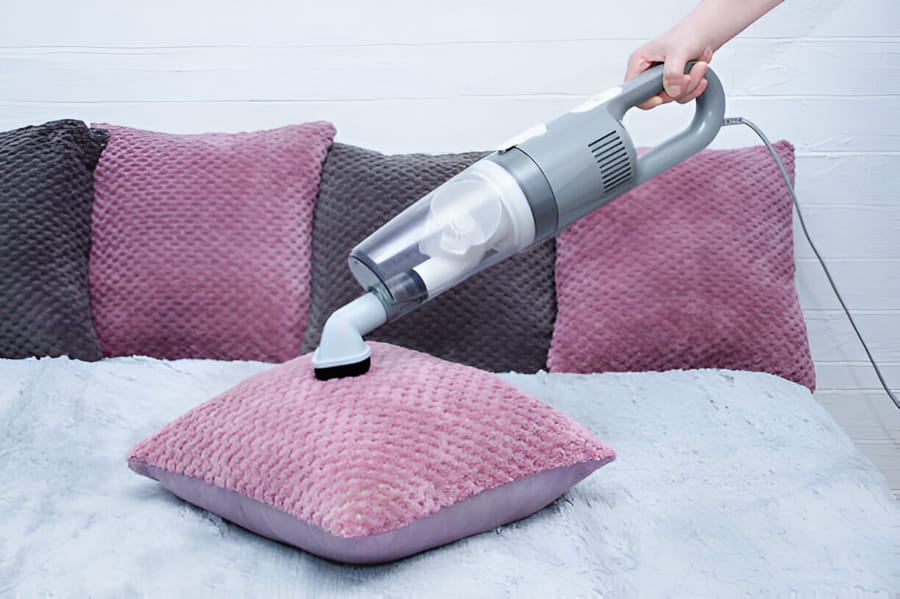 Aspirator de mână utilizat pentru a curăța o pernă roz
