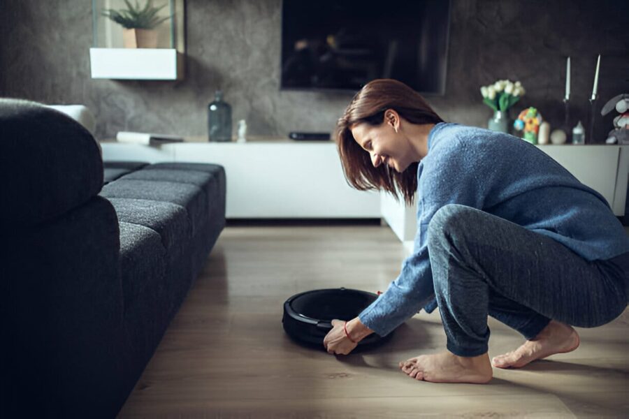 Femeie zâmbind în timp ce reglează aspiratorul robot într-un living luminos