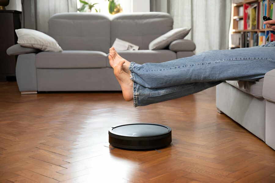 O persoană relaxându-se pe canapea în timp ce un aspirator robot curăță podeaua de lemn