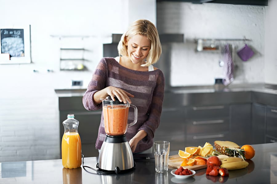 Femeie folosind un blender pentru a prepara un smoothie de fructe