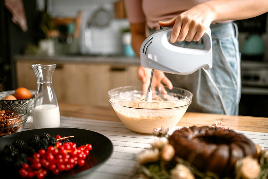 Persoană folosind un mixer de mână pentru a prepara aluat în bucătărie.