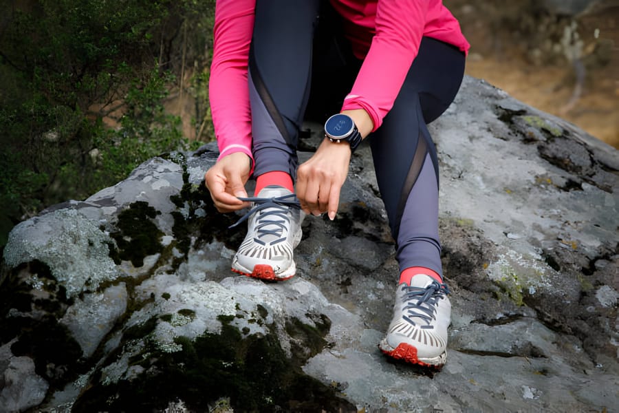 Femeie care își leagă șireturile pantofilor de drumeție pe o piatră în natură.