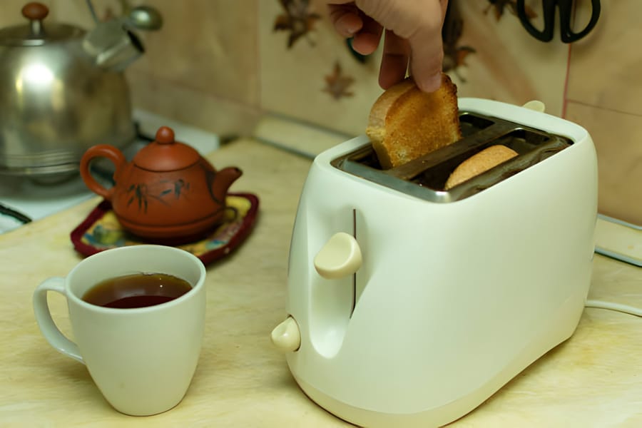 Prăjitor de pâine alb cu felii de pâine prăjite și o ceașcă de ceai