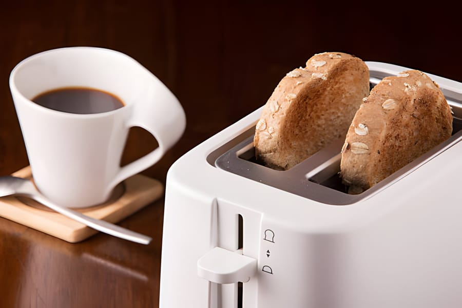 Prăjitor de pâine alb cu felii de pâine integrală și o ceașcă de cafea
