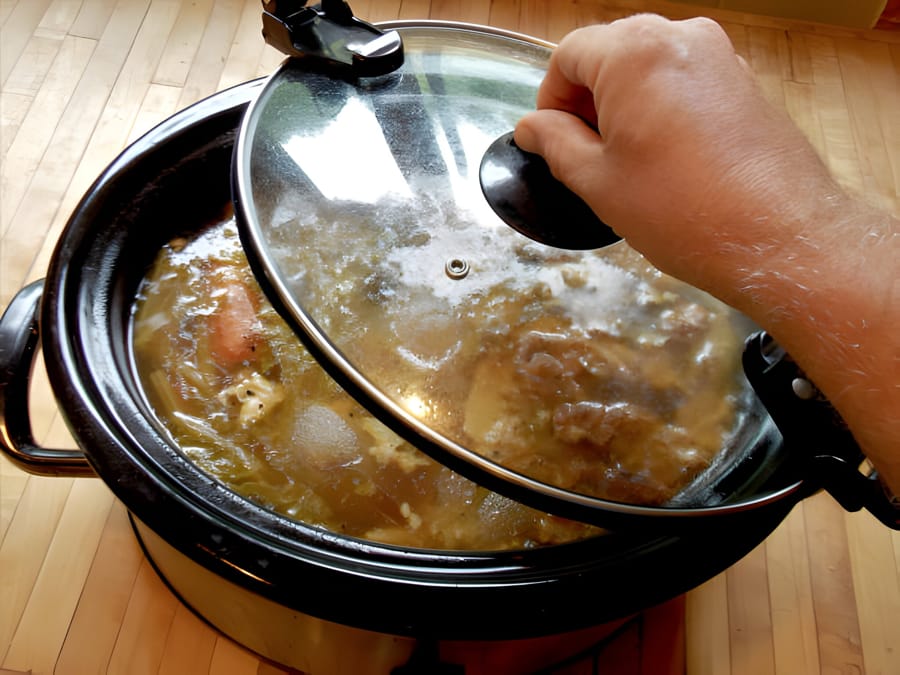 Persoană deschizând capacul unui slow cooker plin cu mâncare