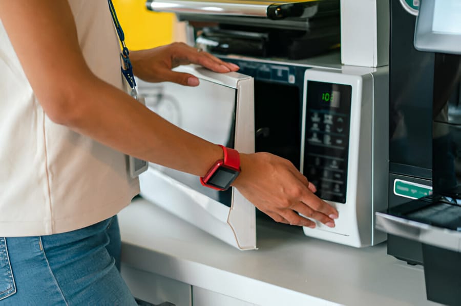 Persoană folosind un cuptor cu microunde într-o bucătărie modernă.