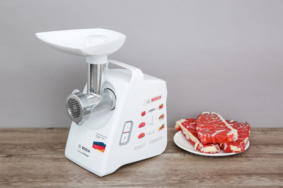Mașină de tocat carne electrică Bosch alături de carne roșie pe o farfurie