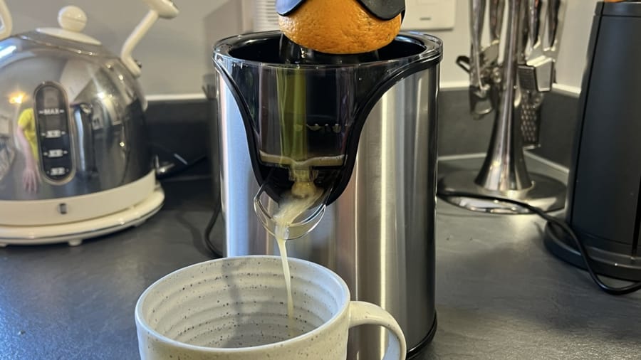 Storcător de citrice în acțiune, stoarcând o portocală într-o cană.