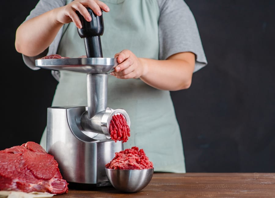 O persoană folosește o mașină de tocat carne electrică din cupru pentru a toca carne proaspătă