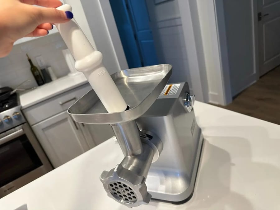 O persoană introduce carne într-o mașină de tocat carne electrică din oțel inoxidabil