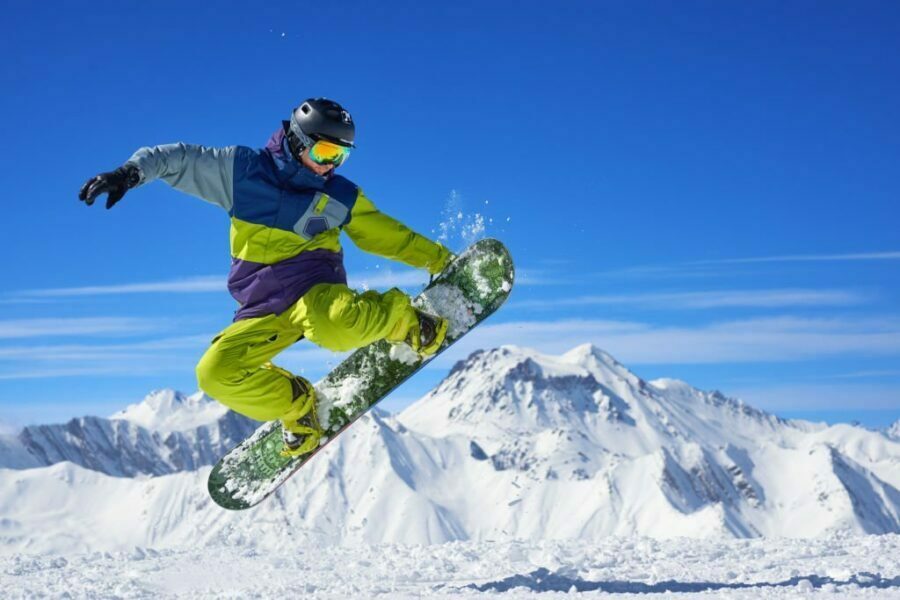 Snowboarder executând un salt cu o placă de snowboard pe un fundal montan înzăpezit