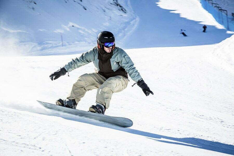 Snowboarder alunecând pe pârtie cu o placă de snowboard, în echipament de protecție