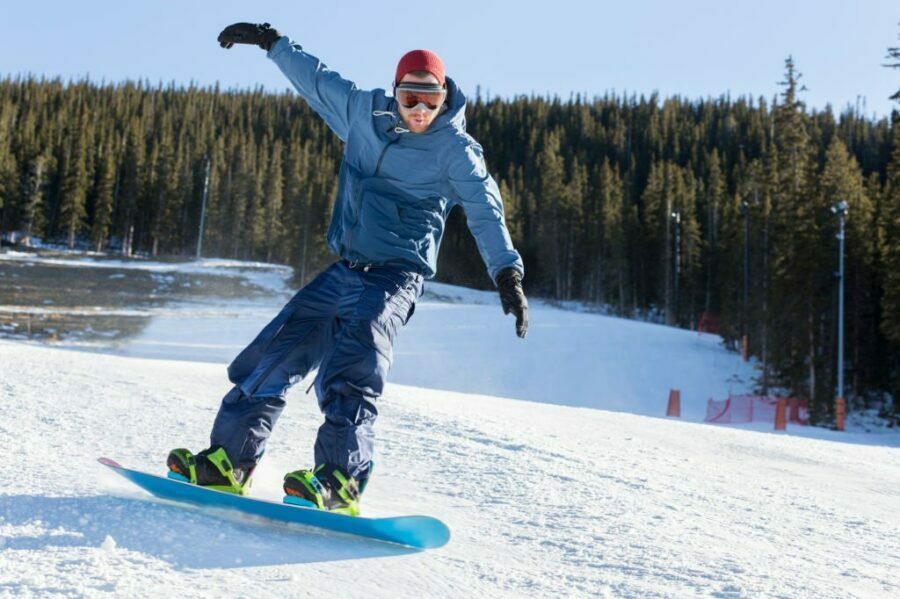 Snowboarder în echipament albastru, efectuând un viraj pe o placă de snowboard pe pârtie