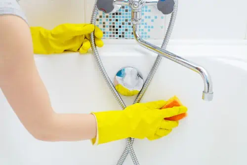 Persoană care curăță o cadă cu mănuși de protecție galbene, folosind o lavetă