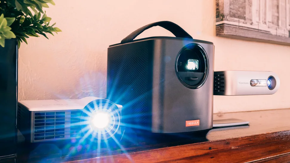 Trei videoproiectoare portabile, inclusiv Nebula și ViewSonic, plasate pe o masă într-un cadru elegant.
