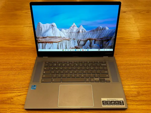 Chromebook Acer deschis pe o masă de lemn, afișând un peisaj montan pe ecran