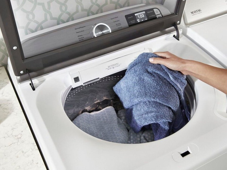 Mână care introduce prosoape într-o mașină de spălat verticală