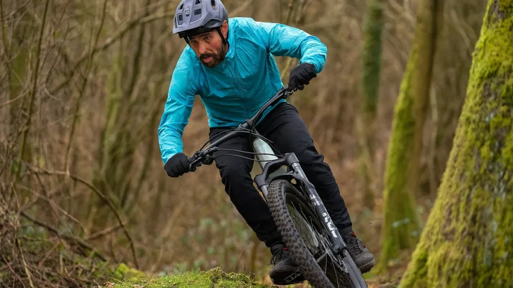 Ciclist pe mountain bike coborând o potecă de pădure, echipat cu cască MTB și jachetă albastră