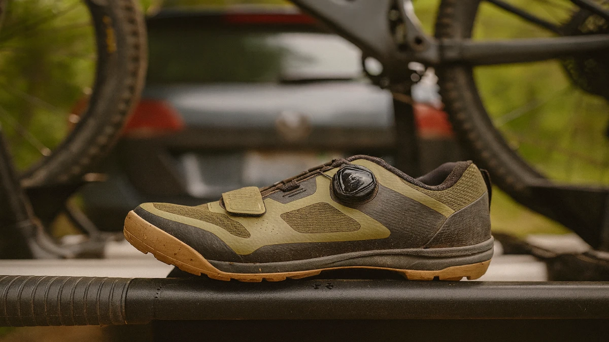 pantof de mountain bike murdar așezat pe suportul unei biciclete, cu mașina și bicicleta în fundal