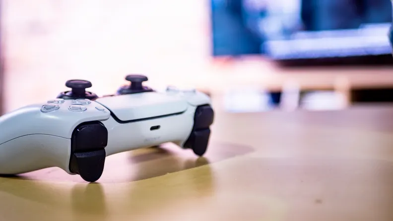 Controller de gaming așezat pe o suprafață din lemn, într-un setup de interior cu fundal estompat